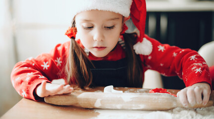 Lovely girl in christmas clothes preparing dough for holidays cookies at home