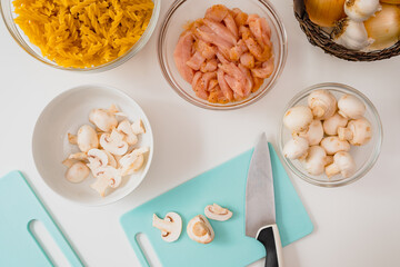 Fresh raw pasta, marinated chicken fillet, mushrooms, onion and garlic. Ingredients close up on white background, view from above