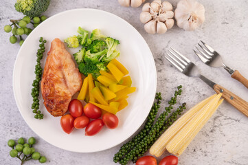 Chicken steak topped with white sesame, peas, tomatoes, broccoli and pumpkin in a white plate.