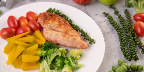 Chicken steak topped with white sesame, peas, tomatoes, broccoli and pumpkin in a white plate.
