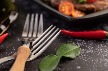 Place a fork on top of each other with chili and kaffir lime leaves on a black background.