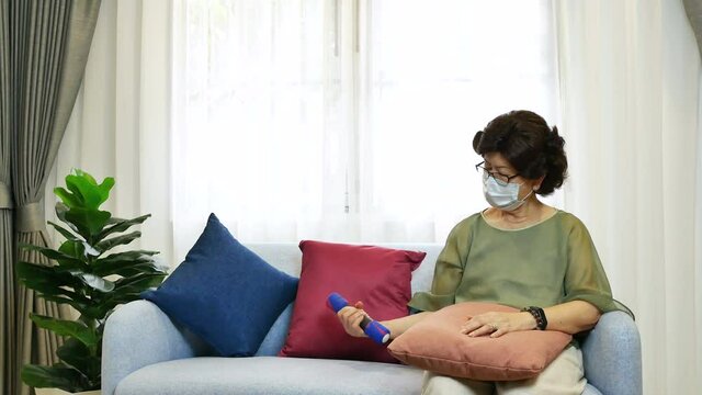 Asian Senior Woman Wearing Face Mask, Sitting On Sofa In Living Room, Lifting Little Dumbbell For Relaxation. Older People Doing Exercise At Home Concept.
