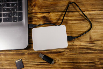 External HDD connected to laptop computer, SD memory card and USB flash drive on a wooden desk. Top...
