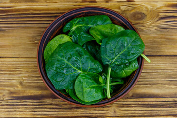Fresh green spinach leaves in bowl on a wooden table. Top view