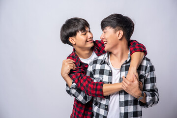 Two men who love each other hug from behind another.