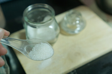 Fototapeta na wymiar Sugar in a spoon, blur glass jar on wooden background