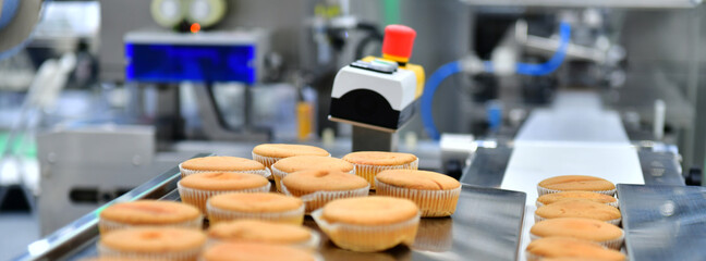 Automatic bakery muffins production line on conveyor belt equipment machinery in factory, industrial food production.