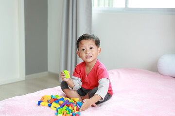 Asian little baby boy playing colorful plastic blocks and lying on bed.