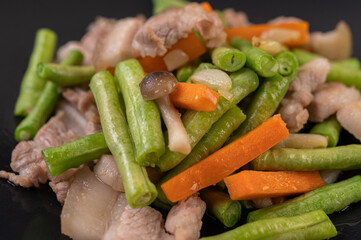 Stir-fried long beans and carrots, add pork belly, put on a black plate.