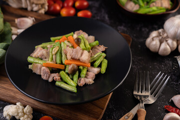 Stir-fried kale and pork belly in a plate placed on a wooden plate.