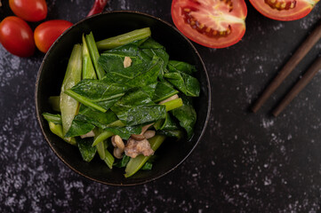 Stir-fried kale and pork belly in a plate placed on a wooden plate.