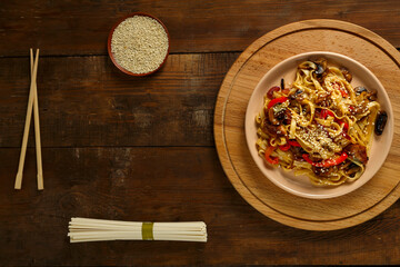 Udon with chicken and mushrooms in pad thai sauce on a plate next to sesame and udon.