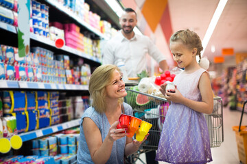 Portrait of smiling woman and girl holding package with yogurt in grocery shop