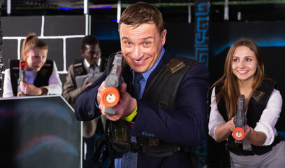 Emotional portrait of businessman playing laser tag with his co-workers on dark gaming arena