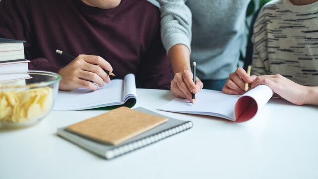 Group of young students tutoring and  catching up workbook with friends