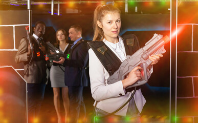Fototapeta na wymiar Emotional portrait of woman playing laser tag with her co-workers in dark room