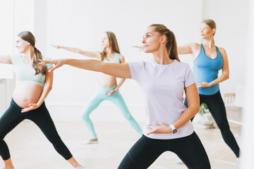 Obraz premium Group of pregnant women in sports uniforms with coach doing gymnastic in the bright studio