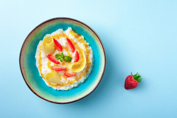Bowl of milk rice porridge with strawberries, mangoes, honey, mint