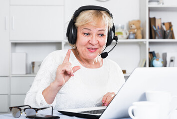 Happy mature woman in headphones with microphone communicating via internet