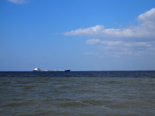 Blue shades horizon. Cargo ship against cloudy blue sky and rippled sea