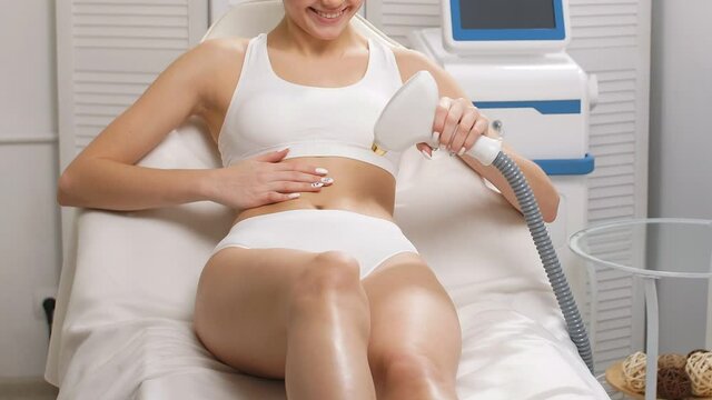 Close-up of slim lady doing laser epilation procedure on her stomach by herself. Cosmetic procedures in beauty spa salon.