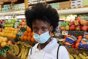 Kid with afro and blue surgical face mask in produce section of grocery store