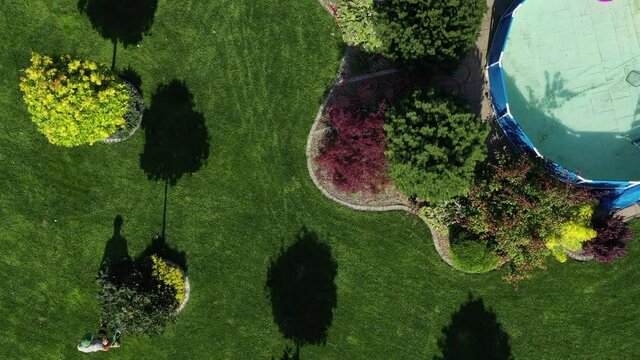 Yard And Garden Work In Summer Concept. Male Worker With Leaf Blower Cleaning Up Freshly Mowed Grass Clippings Stuck Around Trees And Plants. 