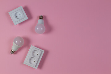 White electrical power sockets, light lamp bulbs on light pink background. Top view