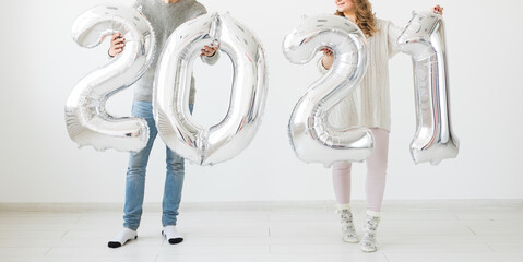 Holidays, festive and party concept - Happy loving couple holds silver 2021 balloons on white background. New Year celebration.