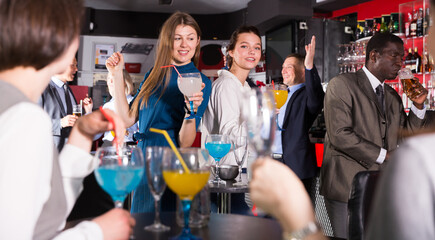 Two smiling girls drinking cocktails and dancing on corporate party