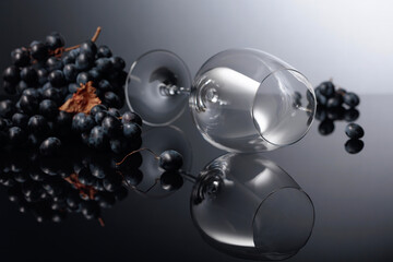 Blue grapes and empty wine glass on a black reflective background.