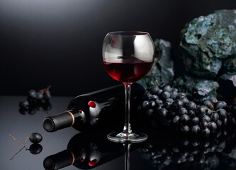Blue grapes and red wine on a black reflective background.