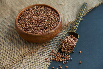 Buckwheat groats in a wooden bowl and vintage scoop. Close up on a black background. copy space for text