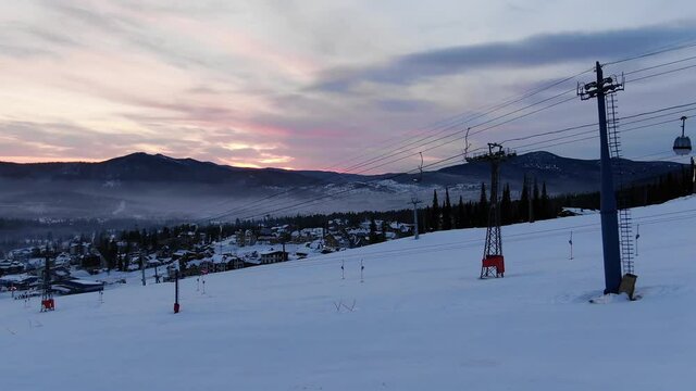 contemporary poma lift transports empty cabins over snowy mountain slope at popular ski resort against evening sky in winter