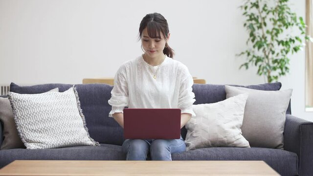 ソファーでラップトップをタイピングする若い女性