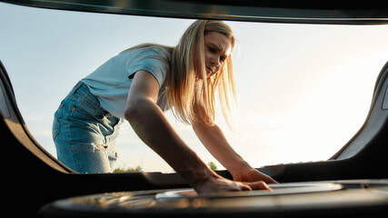 Attractive young woman taking out spare wheel to change on the broken car on her own
