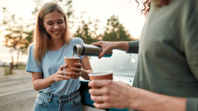 Man pouring coffee or tea from thermos flask, Attractive young woman drinking hot coffee or tea after repairing broken car on the road side