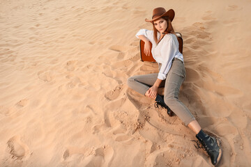 Beautiful fashionable young woman with suitcase in desert