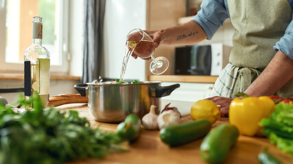 Cropped shot of man, Italian cook pouring a glass of white wine into the pan with chopped...