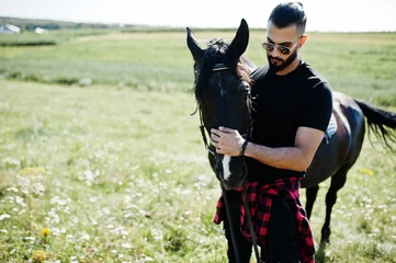 Tuinposter Arab tall beard man wear in black and sunglasses with arabian horse. © AS Photo Family