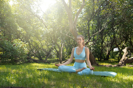 Young  woman in stylish eco friendly sportswear practicing yoga in the greenery park. 