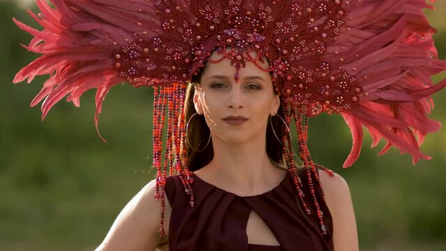 A girl with a red crown of feathers on her head is dancing. Super slow motion