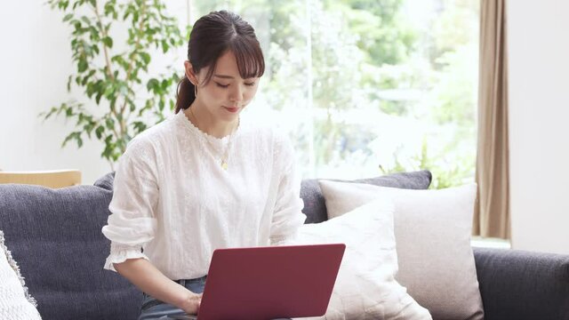 ソファーでラップトップをタイピングする若い女性