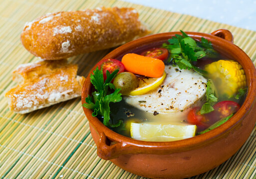 Fisher soup from merluccius. Recipe: boil broth from fish head, add potatoes, carrots, shallots, corn, fish fillets or steak 200 g, season with salt, pepper. Then cook in oven at 200 deg for 40min