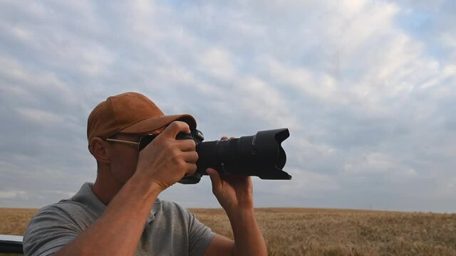 Middle Age Man Standing By Large Field Of Wheat Pointing At Rural Landscape With Camera And Taking Photos. 