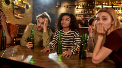Friends looking unhappy while watching sports match on TV together, drinking beer and cheering for team in the bar. People, leisure, friendship and entertainment concept