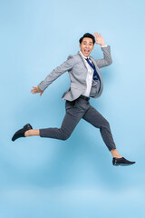 Full length fun portrait of happy energetic young Asian businessman jumping in mid-air isolated on studio blue background