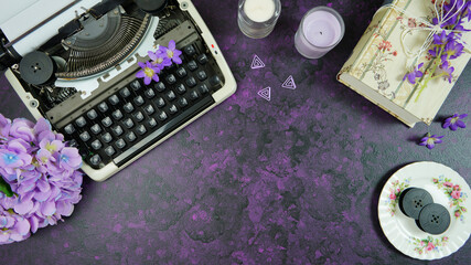Purple theme vintage writers desktop workspace with typewriter, lavendar tea, hibiscus flowers and old books on stylish purple textured background. Top view blog hero header creative flat lay.