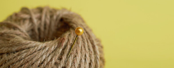 Sewing supplies. Pin stuck in a coil of twine close up on yellow background. Banner