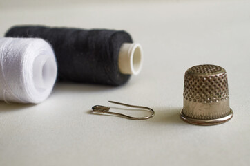 Sewing supplies. Two reels with black and white threads, thimble and pin on a gray background